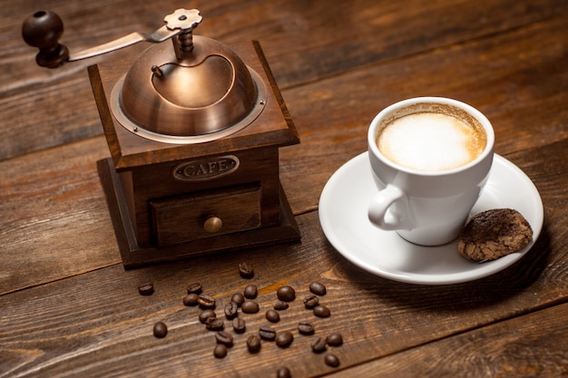 Taza de capuchino molinillo de granos de café sobre mesa de madera