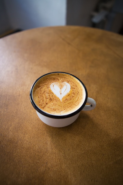 Taza de capuchino con un patrón en forma de corazón sobre una mesa de madera