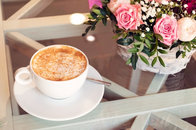 Taza de capuchino y ramo de flores en la mesa de café. Mañana en la gran ciudad.