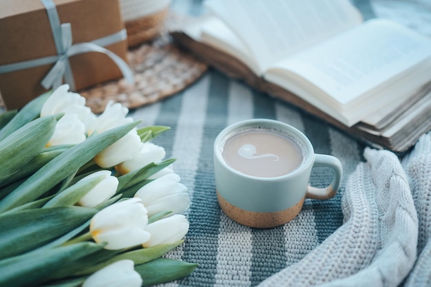 Una taza de capuchino un ramo de tulipanes un libro abierto y un regalo buenos días estética