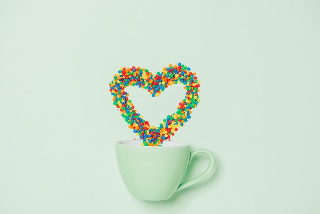 Taza de capuchino con símbolo de forma de corazón y dulces sobre fondo verde pastel