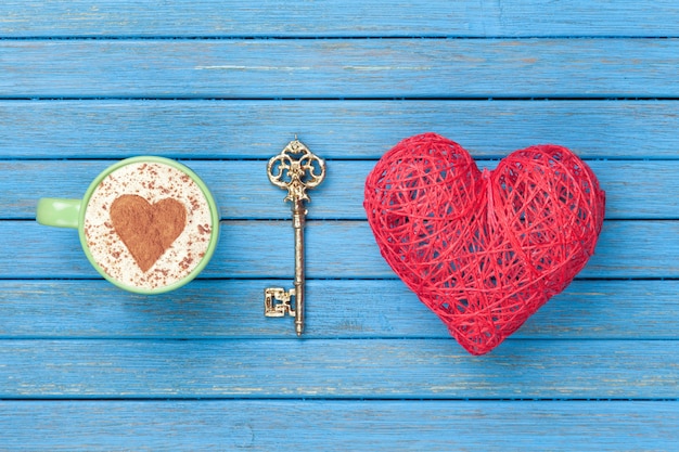 Taza de capuchino con símbolo de forma de corazón, llave y juguete en madera azul.