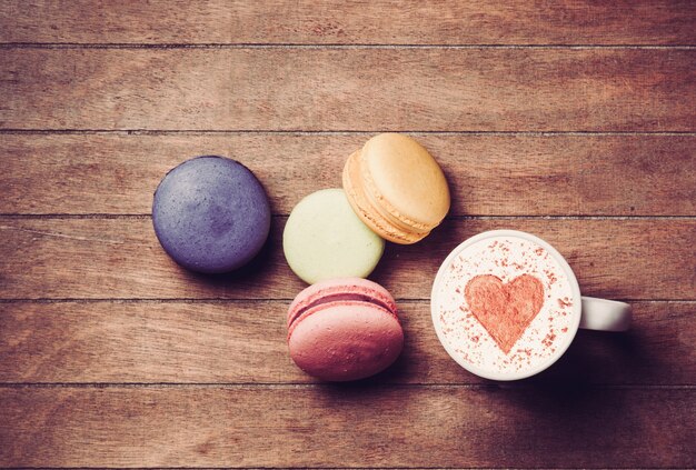 Taza de capuchino con símbolo de forma de corazón y macarons en madera