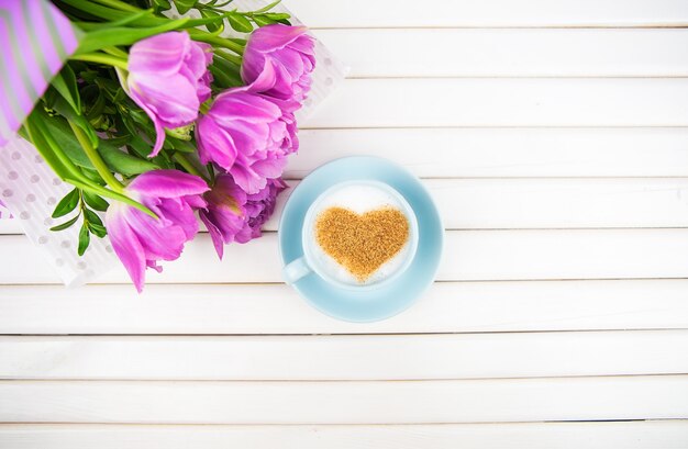 Taza de capuchino con un símbolo en forma de corazón y tulipanes morados sobre un fondo de madera