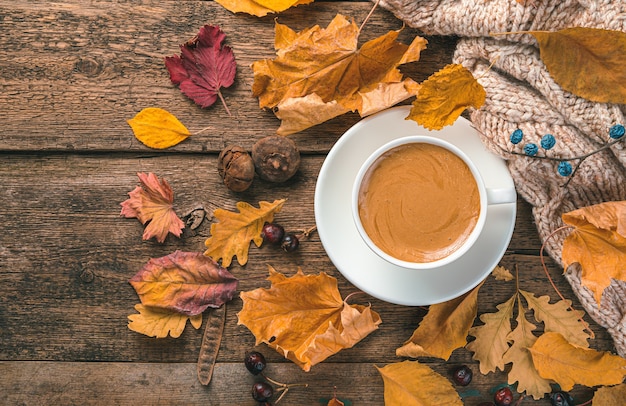 Una taza de capuchino un suéter y follaje otoñal sobre un fondo de madera Fondo de otoño festivo