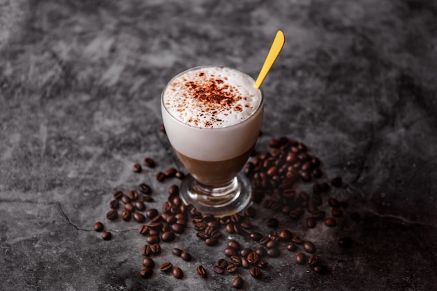 Taza de capuchino en superficie negra. Granos de café tostados con leche caliente, café y cacao en polvo con espacio de copia