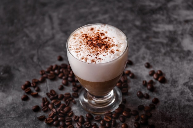 Taza de capuchino en superficie negra. Granos de café tostados con leche caliente, café y cacao en polvo con espacio de copia