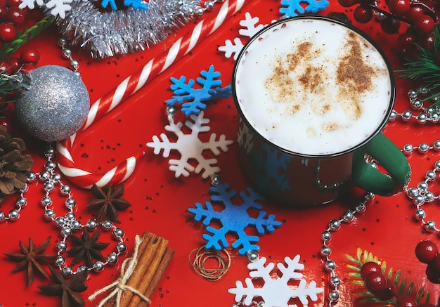 Taza de capuchino verde con adornos navideños sobre un fondo rojo.