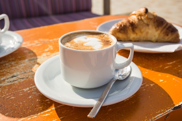 Taza de capuchino vigorizante y croissant para el desayuno