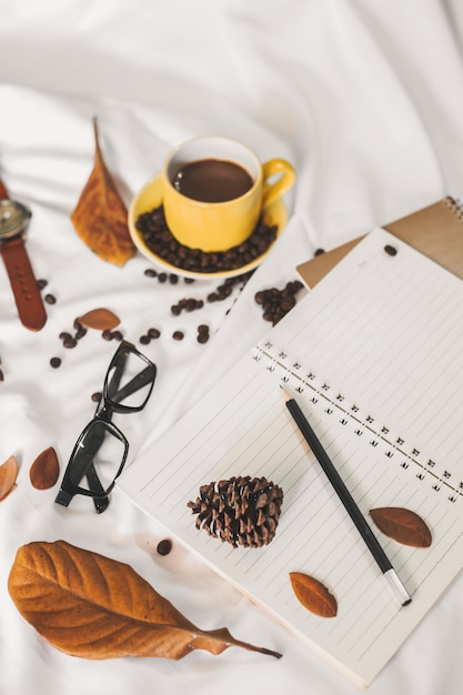 Taza de la carta de la libreta de café y un libro con una manta en una materia textil blanca en cama.