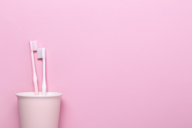 Foto taza con cepillos de dientes rosados y blancos en la pared rosa.