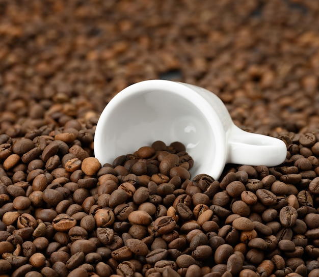 Taza de cerámica blanca se encuentra sobre un montón de granos de café arábica y robusta tostados marrones, full frame