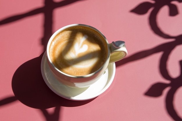 Taza de cerámica con capuchino con un corazón decorado sobre goma espuma en sombras duras sobre un fondo de color