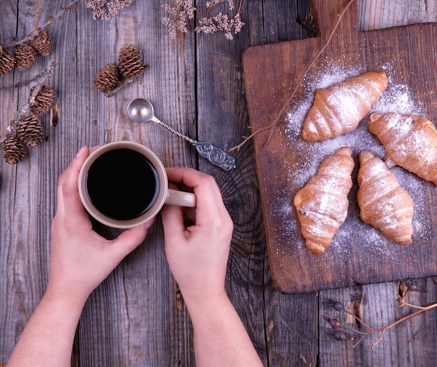 taza de cerámica marrón con café negro y tabla de corte de madera con croissants horneados