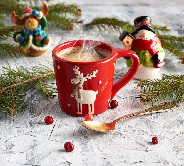 Taza de cerámica roja con café negro cerca de ramas verdes de abeto