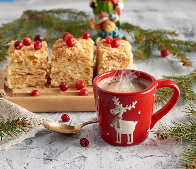 Taza de cerámica roja con café negro y rebanadas de pastel de hojaldre Napoleón con crema de mantequilla