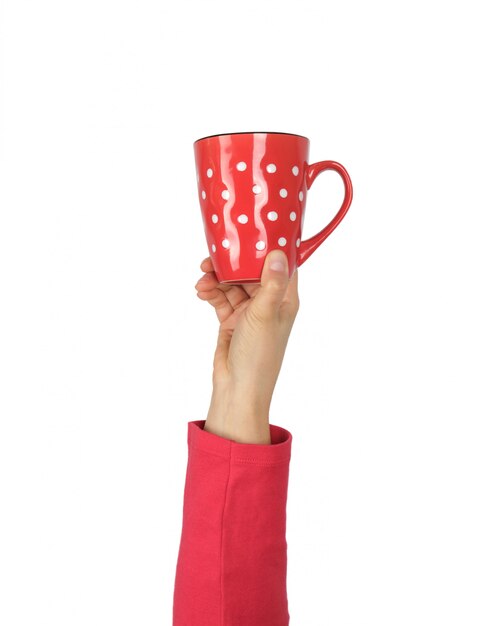 Taza de cerámica roja en una mano femenina sobre un fondo blanco.