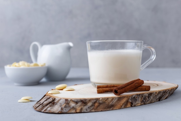 Una taza de chocolate blanco caliente y palitos de canela en un soporte de madera sobre una superficie gris. Keto bebe.