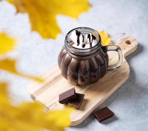 Taza de chocolate caliente aromático con malvaviscos sobre un fondo azul claro con hojas de arce otoñales Bebida acogedora concepto Vista frontal y primer plano