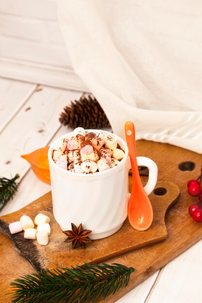 Una taza de chocolate caliente casero en un plato de madera con malvavisco de color