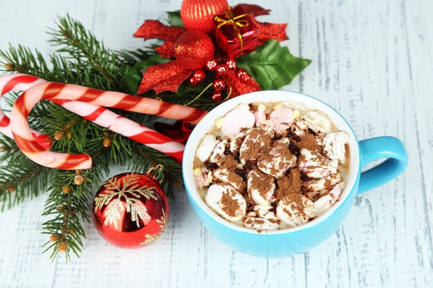 Taza de chocolate caliente con crema en color, sobre la mesa, sobre fondo de adornos navideños