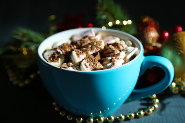 Taza de chocolate caliente con crema en color, sobre la mesa, sobre fondo de adornos navideños