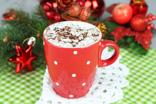 Taza de chocolate caliente con crema en color, sobre una servilleta, sobre fondo de adornos navideños