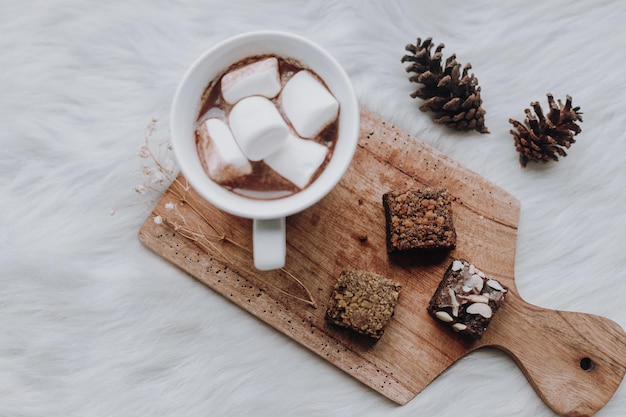 Una taza de chocolate caliente y malvavisco con brownie en bandeja de madera.