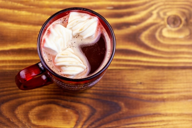 Taza de chocolate caliente con malvavisco derretido sobre mesa de madera