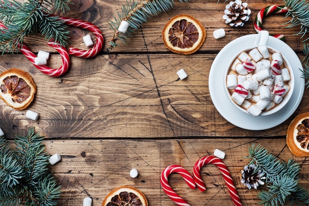 Una taza de chocolate caliente con malvaviscos. Árbol de Navidad y decoraciones, caramelo de caña y naranjas nueces Fondo de madera copia espacio.