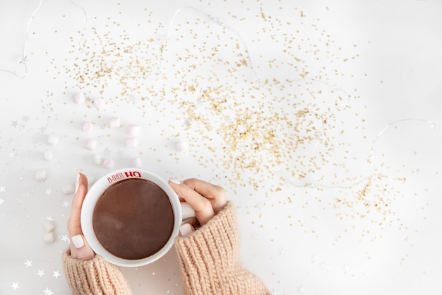 Taza con chocolate caliente en manos sobre un blanco con estrellas brillantes y un gerland