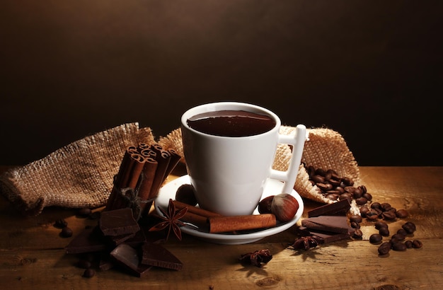 Taza de chocolate caliente, palitos de canela, nueces y chocolate sobre una mesa de madera sobre fondo marrón