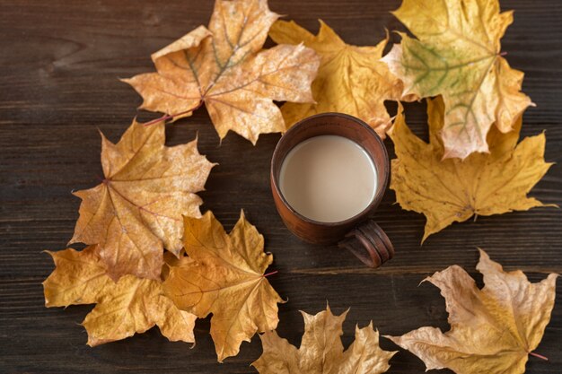 Taza de chocolate caliente sobre fondo de madera en medio de hojas de otoño. Café con leche y hojas de otoño.