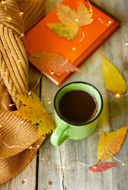 Taza de chocolate caliente sobre una mesa de madera, bodegón con un libro y hojas amarillas y guirnaldas