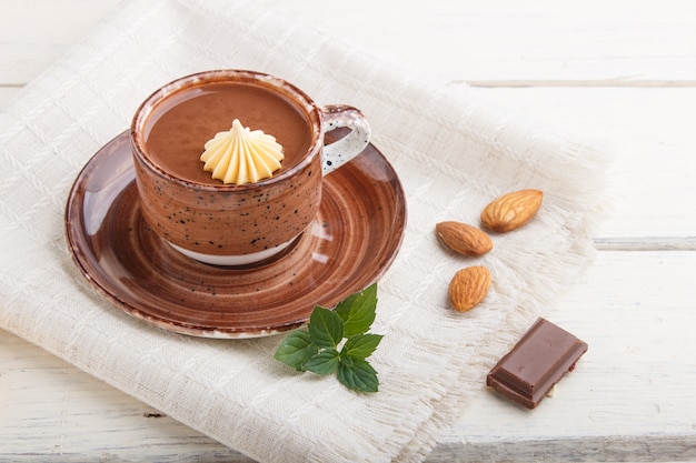 Taza de chocolate caliente y trozos de chocolate con leche con almendras sobre una superficie de madera blanca con servilleta de lino. vista lateral