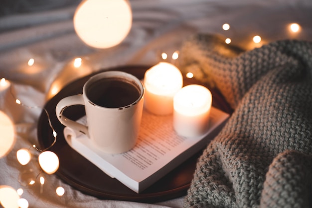 Taza de chocolate caliente con velas encendidas y tejidos de punto en la cama de cerca. Noche. Temporada de vacaciones de invierno.