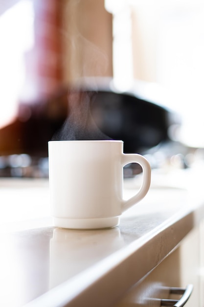 Taza cilíndrica blanca en la mesa de la cocina con luz natural real