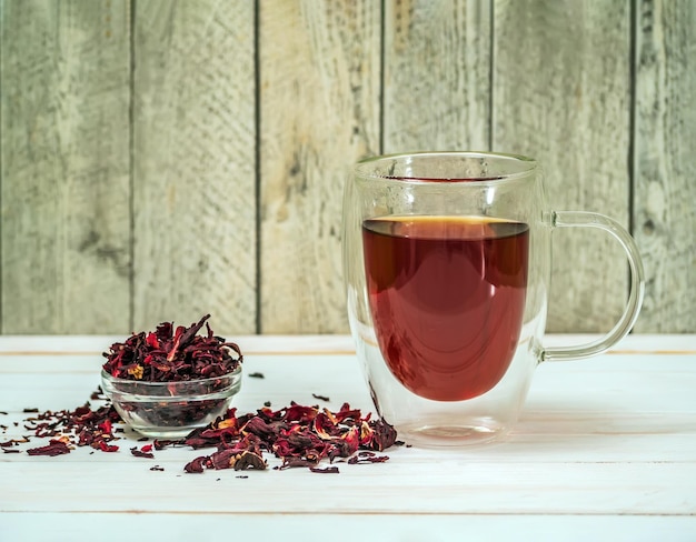 Foto taza clara de doble pared llena de té caliente de hibisco con hojas secas de hibisco