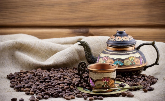 Taza de cobre y tetera con montón de granos de café.