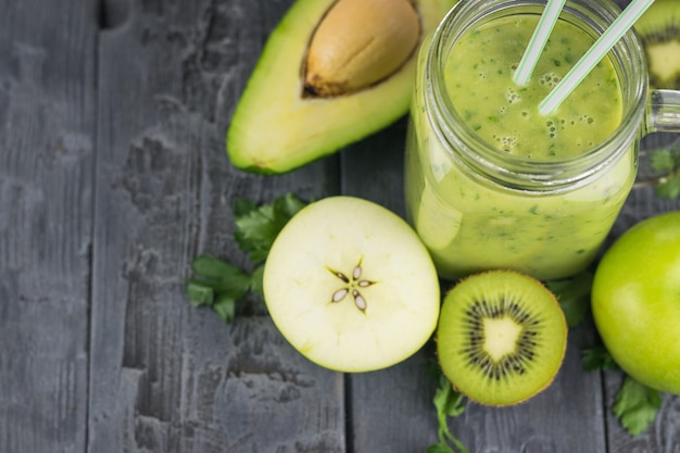 Taza con un cóctel de aguacate batido recién preparado con dos pajitas en una mesa de madera