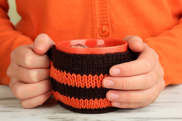 Taza con cosa tejida en manos femeninas de cerca