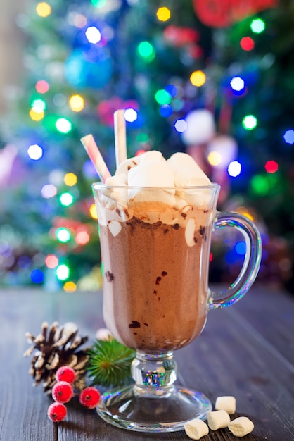 Taza de cristal de chocolate caliente con mini malvaviscos con ramas de pino, un fondo rústico