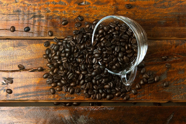 La taza de cristal con los granos de café asados y frescos vertió sobre la tabla de madera rústica. Vista superior