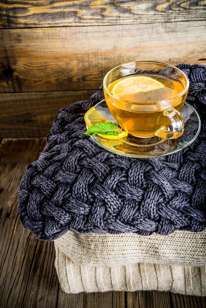 Taza de cristal de té con limón, menta y especias, en la vieja mesa de madera rústica con mantas calientes.