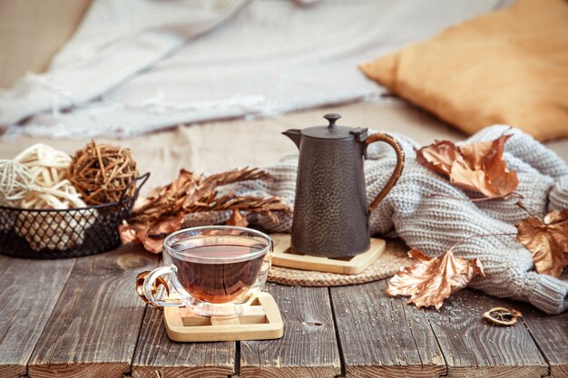 Taza de cristal con té y tetera en mesa de madera con detalles de decoración otoñal de cerca.