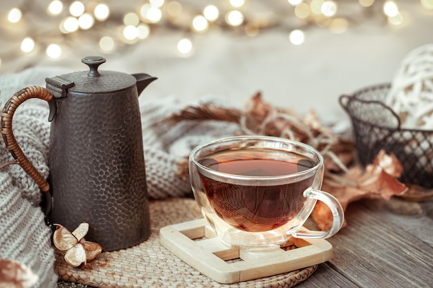 Taza de cristal con té y tetera en mesa de madera con detalles de decoración otoñal de cerca.