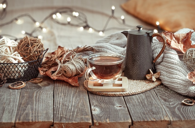 Taza de cristal con té y tetera en mesa de madera con detalles de decoración otoñal.