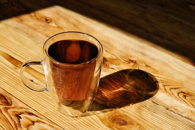 Taza de cristal transparente de té negro caliente en la mesa de madera