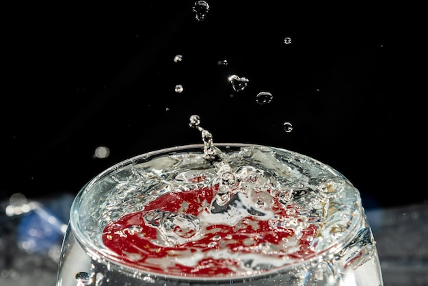 Foto taza de vidro transparente cheia de água com reflexo vermelho e gotas de salpicaduras efeito de salpicadura