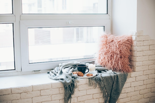 Taza de desayuno de estilo escandinavo con café y galletas en un acogedor alféizar con una manta cálida